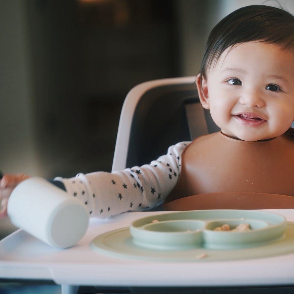 Baby boy enjoying breakfast using the bib, straw cup and suction mini mat from the Family Flavors Mealtime Kit